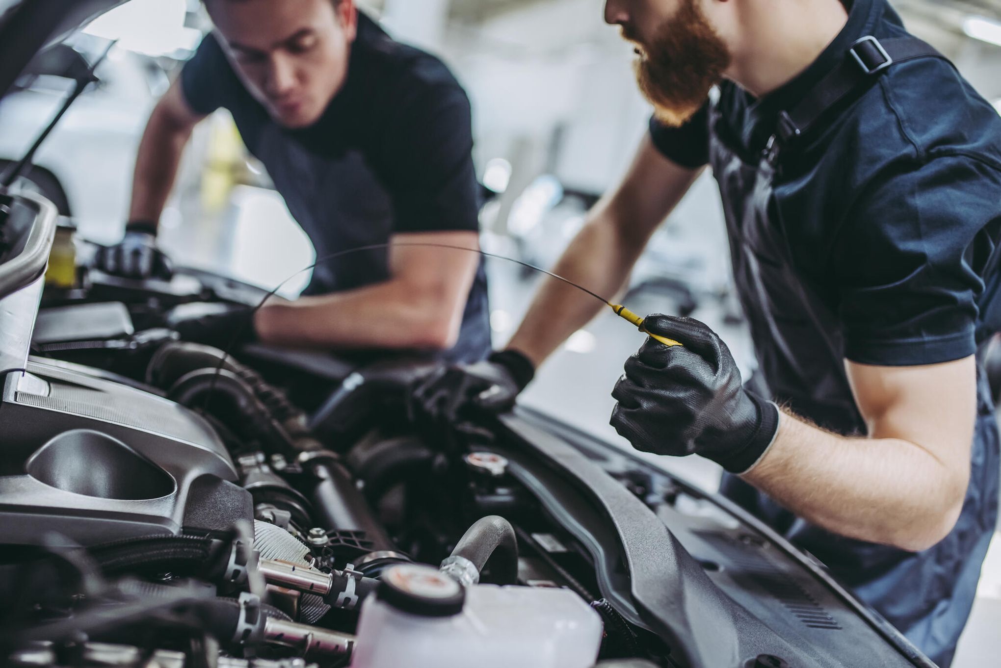 Zwei Mechaniker stehen vor einer geöffneten Motorhaube und kontrollieren den Ölstand